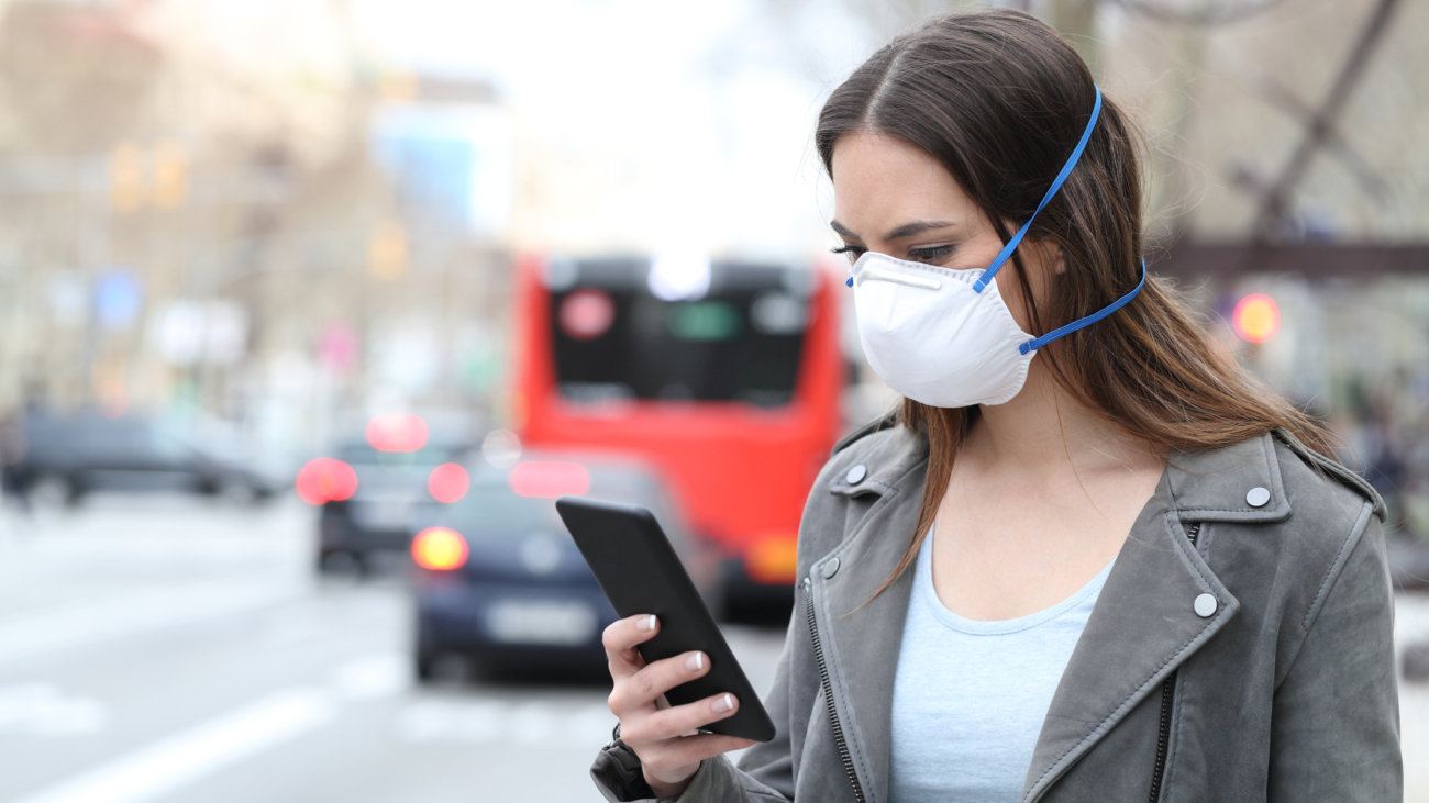 Woman with mask using phone with city traffic background